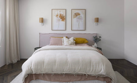 Lavender coloured linen slipcover bed head dressed in gingham sheets and framed by pastel artwork