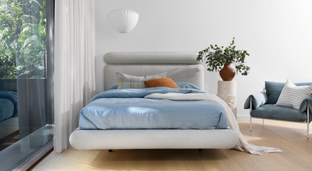 Upholstered Bed Base that's floating above oak flooring and draped in soft blue linen
