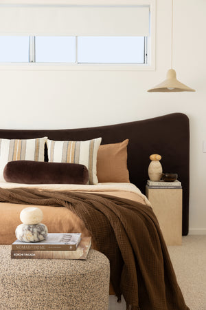 Cozy bedroom with chocolate oversized bedhead, striped pillows, brown blanket, and a side table with decor items.