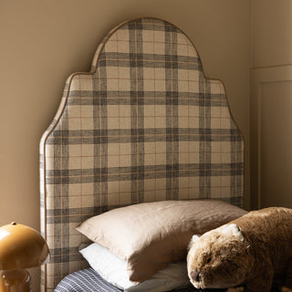 Plaid headboard with pillows and a teddy bear on a bed against a beige wall.