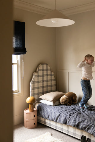Child playing on a bed in a bedroom with plaid headboard and bedding.