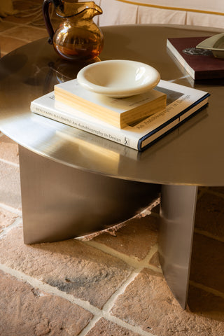 Round stainless steel coffee table with books and a bowl on a stone floor