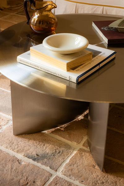 Round stainless steel coffee table with books and a bowl on a stone floor