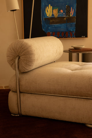Occasional chair with round back rest and stainless steal detail in a room with a painting on the wall.