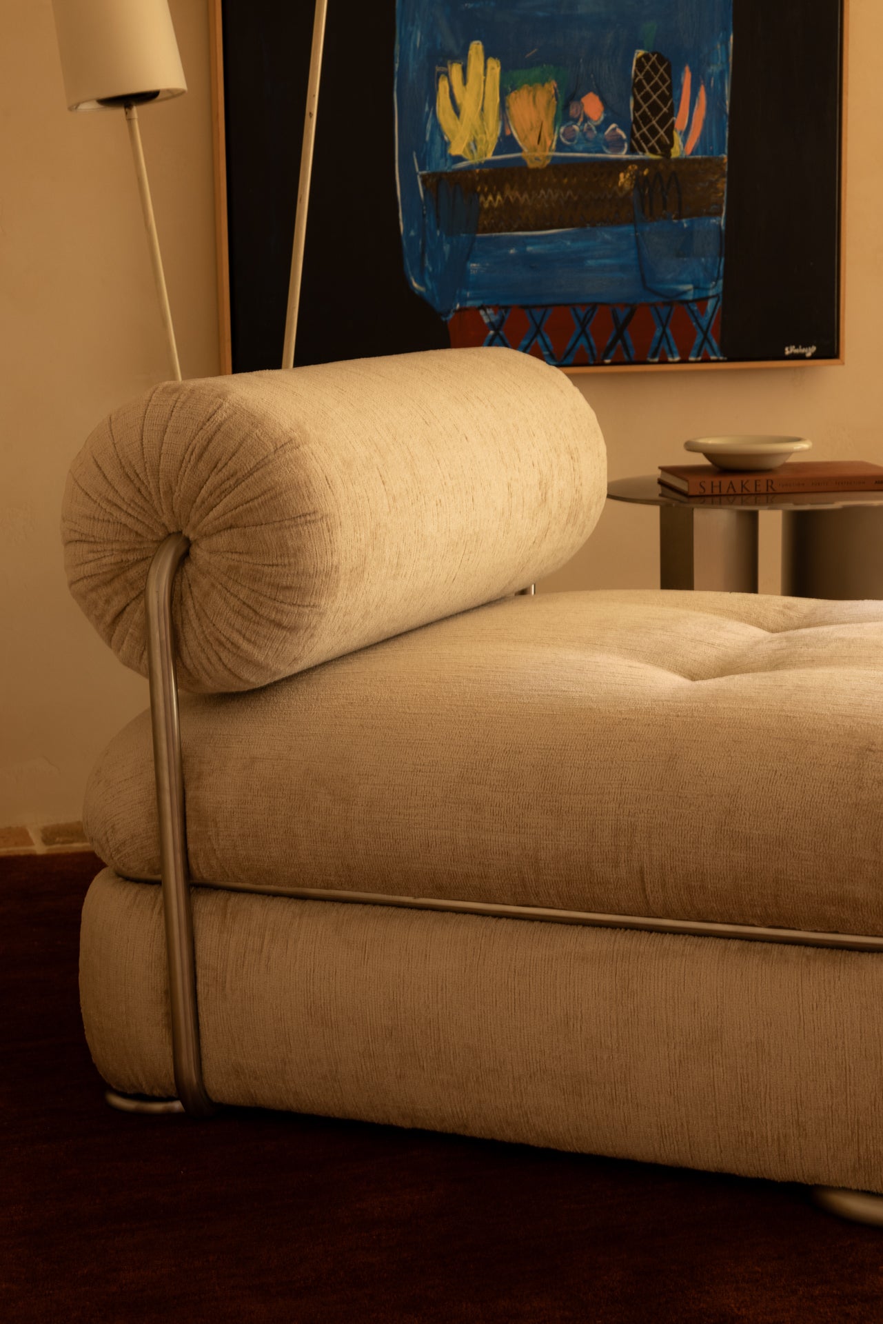 Occasional chair with round back rest and stainless steal detail in a room with a painting on the wall.