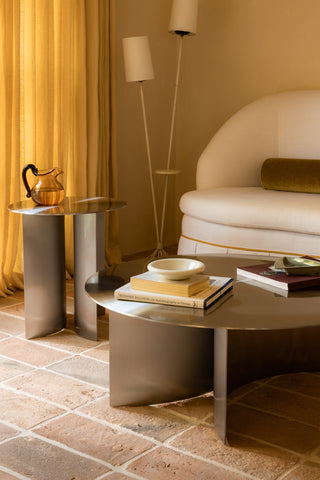 Modern living room with a round stainless steel coffee table, chair, and decorative items.