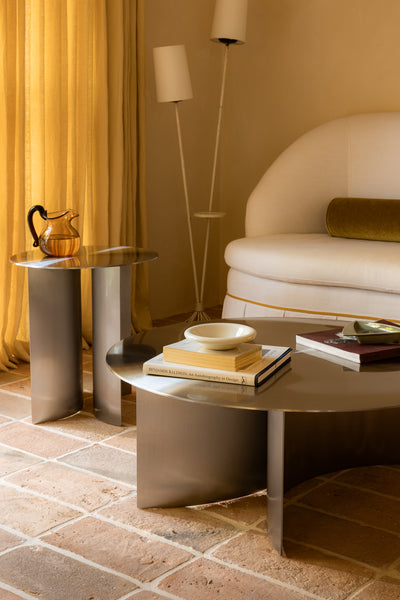Modern living room with a round stainless steel coffee table, chair, and decorative items.