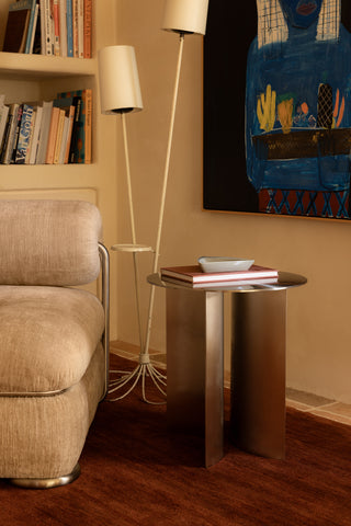 Living room with beige armchair, stainless steel side table, lamp, and colorful painting on wall.