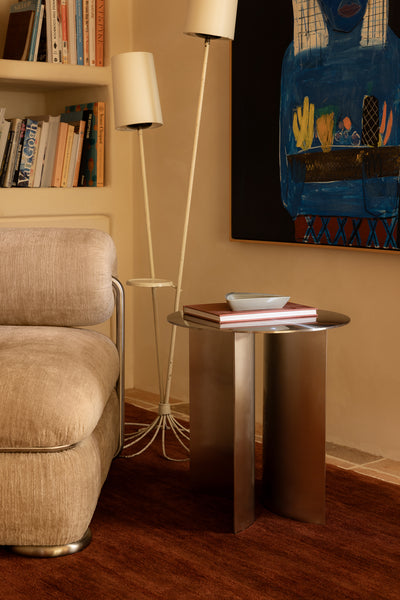 Living room with beige armchair, stainless steel side table, lamp, and colorful painting on wall.