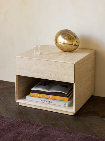 Travertine side table with books and a gold sphere on a wooden floor.