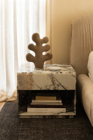 Marble-patterned side table with drawer, styled with books and a sculpture next to a bed.