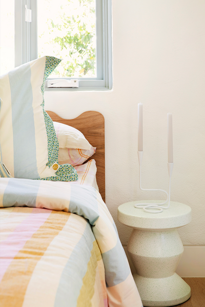 Floating girls bed in timber with curved rails and dressed in striped linen sheets