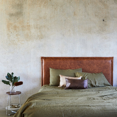 leather bed head made in Australia by Create Estate, pictured with green linen sheets on a concrete wall