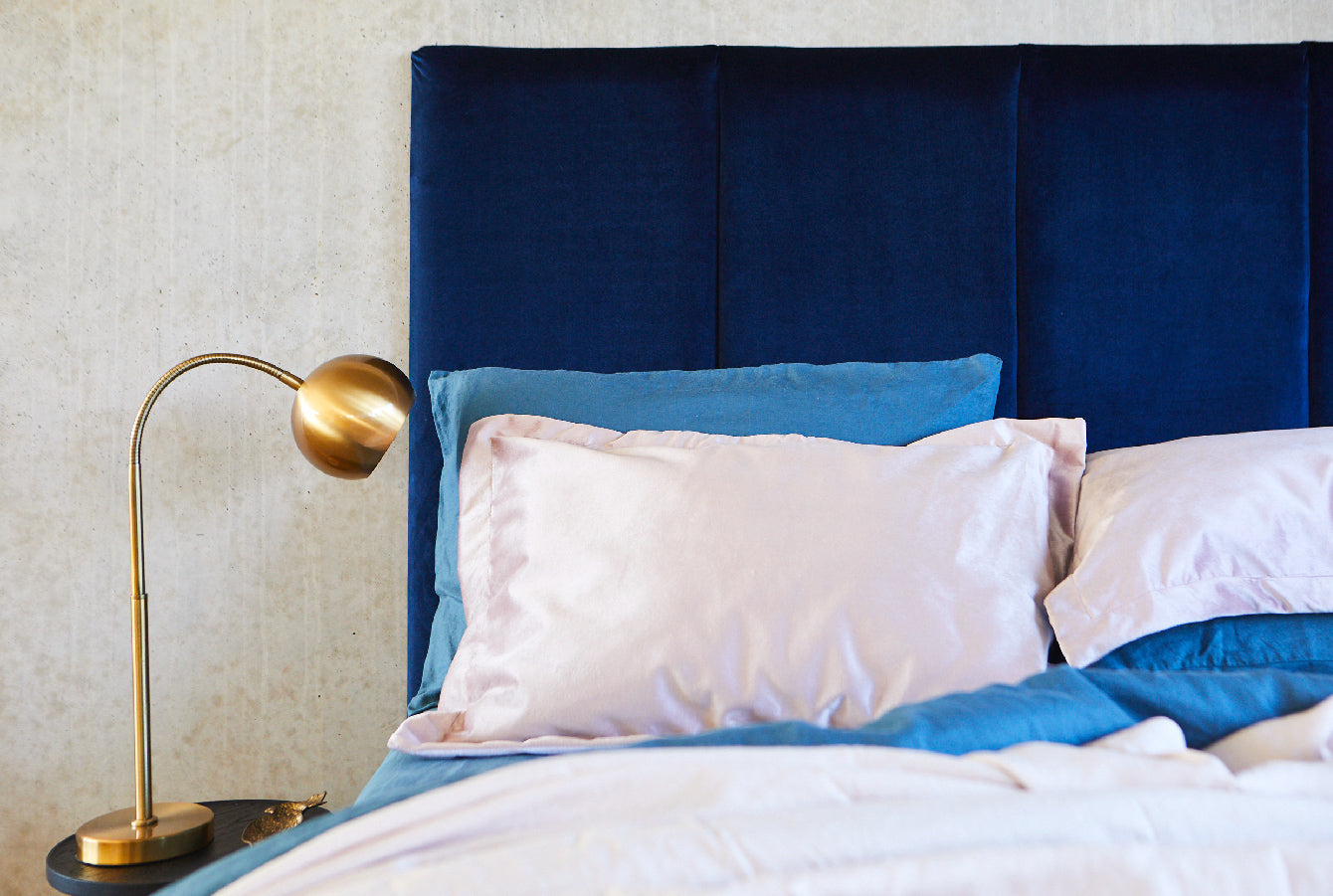 Blue velvet bed head pictured with blue linen sheets against a concrete bedroom. Made in Australia by Create Estate