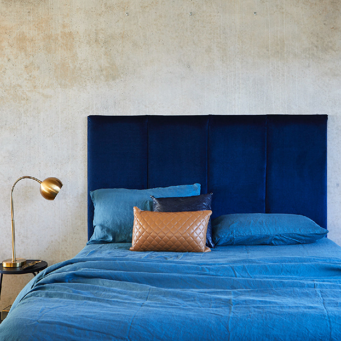 Blue velvet bed head pictured with blue linen sheets against a concrete bedroom. Made in Australia by Create Estate